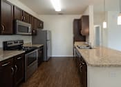 Thumbnail 7 of 21 - A kitchen with dark brown cabinets and a granite countertop.
