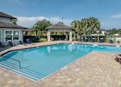 Thumbnail 6 of 21 - A swimming pool surrounded by a brick patio and a gazebo.