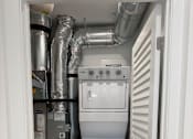 Thumbnail 10 of 24 - A white washing machine is in a small room with a wall of pipes.