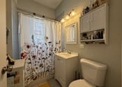 Thumbnail 3 of 8 - A small white bathroom with a floral shower curtain.