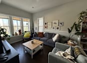 Thumbnail 7 of 8 - A living room with a grey couch, a wooden coffee table, and a large window.