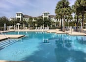 Thumbnail 14 of 44 - A large swimming pool in front of a building with palm trees.