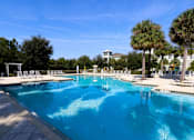 Thumbnail 12 of 44 - A large swimming pool with a white fence and chairs around it.