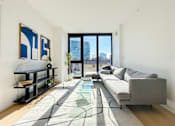 Thumbnail 21 of 84 - A modern living room with a grey sofa, a glass coffee table, and a large window with a view of the city.