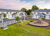 Thumbnail 6 of 18 - A playground with a slide and a swing set in the middle of a grassy area.