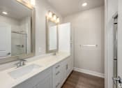 Thumbnail 12 of 18 - A bathroom with a sink, mirror, and wooden floors.
