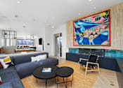 Thumbnail 5 of 44 - A living room with a grey couch, a black coffee table, and a large abstract painting on the wall.
