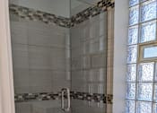 Thumbnail 9 of 19 - A shower with a glass door and a tiled floor.