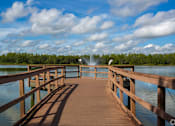 Thumbnail 23 of 24 - A wooden pier extends into a body of water with a fountain in the distance.