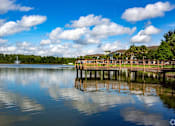 Thumbnail 44 of 44 - A wooden pier extends into a calm body of water under a blue sky with scattered clouds.