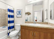 Thumbnail 28 of 71 - A bathroom with a white toilet, a white sink, a blue and white striped shower curtain, and a wooden cabinet.
