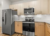 Thumbnail 24 of 50 - A kitchen with a refrigerator, microwave, oven, and cabinets.