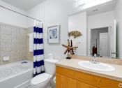 Thumbnail 49 of 71 - A bathroom with a white toilet, a white sink, a white bathtub, a blue and white striped shower curtain, a starfish decoration, and a mirror.