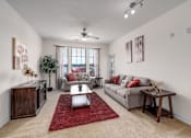 Thumbnail 44 of 71 - A living room with a grey couch, a red rug, and a ceiling fan.