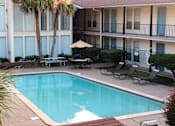 Thumbnail 7 of 12 - A pool surrounded by chairs and a building with blue doors.