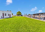 Thumbnail 15 of 23 - A large grassy field with a building and a tree in the background.