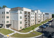 Thumbnail 9 of 20 - A row of modern apartment buildings with cars parked in the lot.