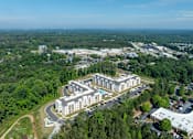 Thumbnail 2 of 20 - An aerial view of a large building surrounded by trees and a parking lot.