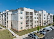 Thumbnail 8 of 20 - A large apartment complex with a parking lot in front.