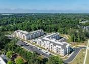 Thumbnail 4 of 20 - A large white building surrounded by trees and a parking lot.