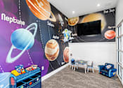 Thumbnail 38 of 41 - A room with a mural of planets on the wall and a blue sofa.