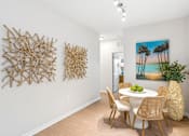 Thumbnail 28 of 41 - A dining room with a white table and chairs, a painting of a beach scene, and two pieces of artwork on the wall.