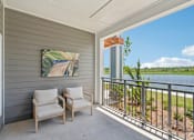 Thumbnail 33 of 41 - Two chairs are on a porch with a painting and a view of a lake.