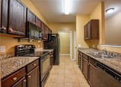Thumbnail 18 of 26 - A kitchen with brown cabinets and black appliances.