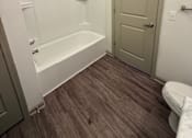 Thumbnail 17 of 17 - A white bathtub with a shower head is in a bathroom with a toilet and a door.