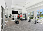 Thumbnail 19 of 41 - A spacious gym with a variety of exercise equipment and a view of the pool outside.
