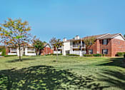 Thumbnail 1 of 20 - A large grassy field with a tree and apartment buildings in the background.