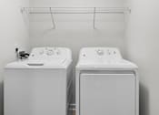 Thumbnail 5 of 26 - Two white front loading washing machines in a laundry room at Grand at Pearl Apartments, Mississippi
