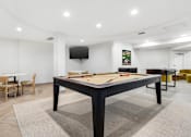 Thumbnail 2 of 26 - A billiard table is in the middle of a room with a TV mounted on the wall.