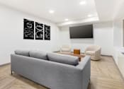 Thumbnail 7 of 26 - A grey couch sits in a living room with a television and two chairs.