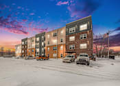Thumbnail 2 of 30 - A row of apartment buildings with cars parked in front.