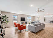Thumbnail 21 of 30 - A living room with a grey couch, orange chairs, and a ceiling fan.