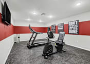 Thumbnail 26 of 31 - A gym room with a treadmill and a stationary bike.
