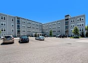 Thumbnail 34 of 40 - an apartment building in a parking lot with cars
