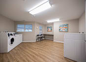 Thumbnail 52 of 58 - A laundry room with a washer and dryer, a chair, and two paintings on the wall.