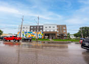 Thumbnail 51 of 58 - A red car is parked in front of a building with a colorful mural on the side.