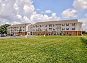Thumbnail 44 of 56 - A large apartment complex with a grassy field in front.