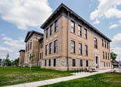 Thumbnail 24 of 58 - A large, two-story building with a flat roof and a mix of stone and brick exterior.