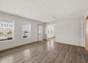 Thumbnail 17 of 43 - A spacious room with wooden floors and white walls, featuring two windows with pictures on them.