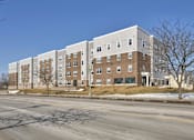 Thumbnail 1 of 18 - A large multi-story building with a flat roof and a parking lot in front.