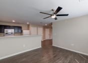 Thumbnail 7 of 26 - an empty living room with a ceiling fan and a kitchen in the background
