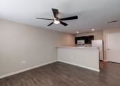 Thumbnail 11 of 26 - an empty room with a ceiling fan and a kitchen in the background
