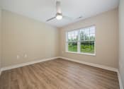 Thumbnail 11 of 48 - A room with a ceiling fan and a window overlooking a green area.