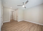 Thumbnail 22 of 48 - A room with a ceiling fan and light fixture, hardwood floors, and a doorway leading to another room.