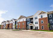 Thumbnail 34 of 48 - A large apartment complex with multiple buildings and parking spaces in front.