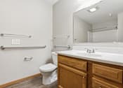Thumbnail 51 of 66 - A white toilet sits in a bathroom with a white sink and wooden cabinets.